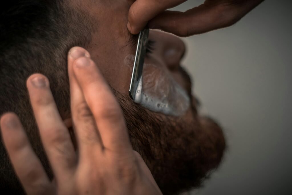 Detailed close-up image of a barber using a razor for precise beard trimming in the barbershop.